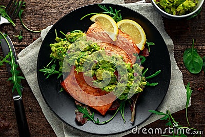 Oven cooked salmon steak, fillet with avocado salsa and green on black plate. wooden table. healthy food Stock Photo