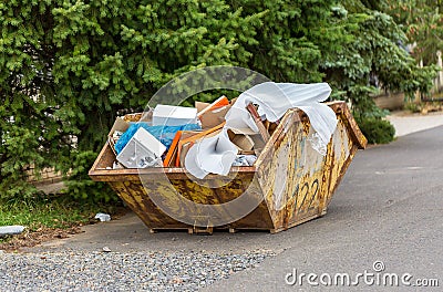 Overflowing rusty metal container for construction waste with cardboard boxes and plastic trash Stock Photo