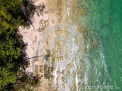 Overhead drone view of a small tropical beach surrounded by palm trees and shallow ocean Stock Photo