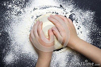 An overhead photo of kid`s hands, some sprinkled flour and wheat dough on the black table with a place for text. Child`s hands m Stock Photo