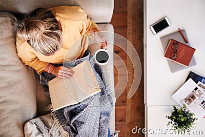 Overhead Shot Looking Down On Woman At Home Lying On Reading Book And Drinking Coffee Stock Photo