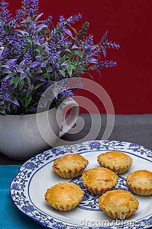 An overhead shot of mini pies in a china plate next to a white vase full of lavender Stock Photo