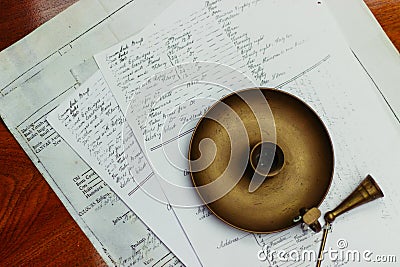 Overhead shot of a n old metal candle holder placed on printed sheets of paper on a brown table Stock Photo