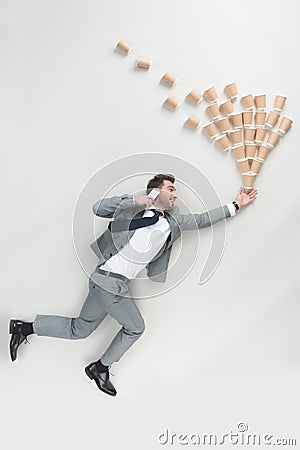 overhead view of businessman talking on smartphone while holding pile of disposable cups Stock Photo