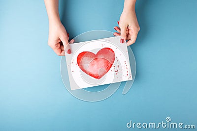 Female hands holding card with heart on blue background. Stock Photo