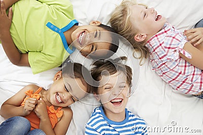 Overhead View Of Four Children Playing On Bed Together Stock Photo