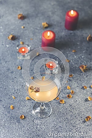 Overhead view of grapefruit martini cocktail with dried roses flowers and petals, surrounded candles on dark gray table surface Stock Photo