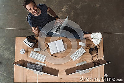 overhead view of handsome young programmer using laptop and smiling Stock Photo