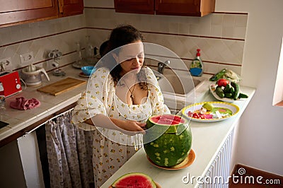 Overhead View of a pleasant housewife cutting ripe organic juicy watermelon in the rustic home kitchen interior Stock Photo