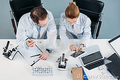 overhead view of scientific researchers in white coats using tablet together at workplace Stock Photo