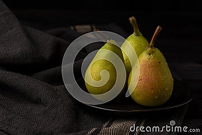 Overhead view of three green pears with water drops in black plate on dark table Stock Photo