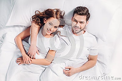 overhead view of young smiling couple in love lying on bed under Stock Photo