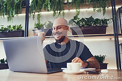 Overjoyed businessman or student uses laptop in cafe shows yes gesture while looks at laptop screen Stock Photo