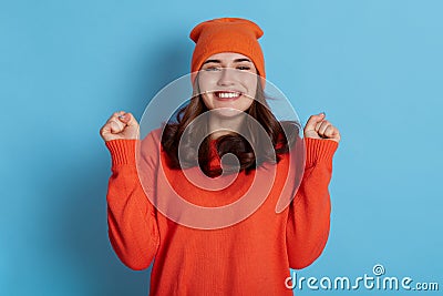Overjoyed dark haired European young lady clenches two fists celebrates success and exclaims with joy makes hooray gesture Stock Photo