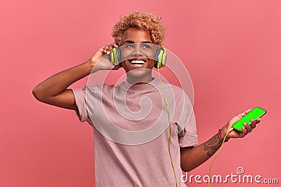 Overjoyed dark skinned girl stays alive with sound of music, keeps hands on headphones, has modern gadgets, listens song Stock Photo