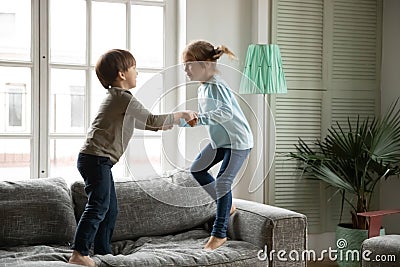 Overjoyed little boy and girl holding hands, jumping on couch Stock Photo