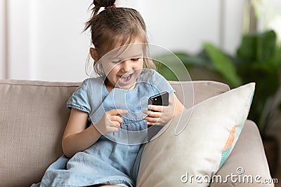 Overjoyed little preschool kid girl playing online game on smartphone. Stock Photo