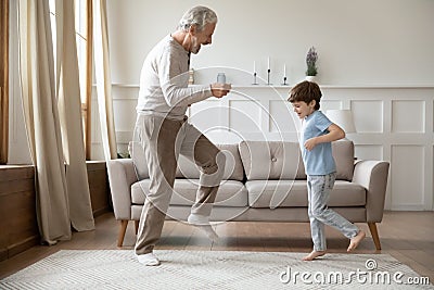 Overjoyed older senior grandfather dancing with excited little grandson. Stock Photo