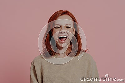 Overjoyed red-haired woman laughing positively, with closed eyes, isolated on pink background Stock Photo