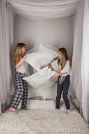 Overjoyed young mom and happy little daughter have fun engaged in pillow fight in bedroom, excited mother and small preschooler Stock Photo