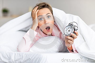 Overleeping. Portrait of shocked woman holding clock in bed Stock Photo