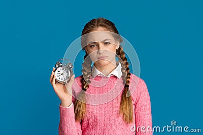 Oversleep concept. Tired teenager girl with pigtails holds alarm clock in her hands Stock Photo