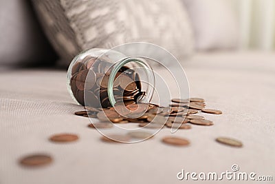Overturned glass jar with coins on grey sofa Stock Photo