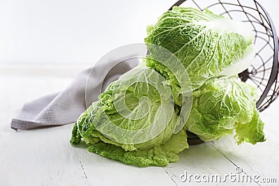 Overturned metal basket with fresh ripe cabbage on light wooden table Stock Photo