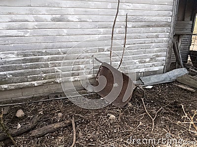 Overturned metal wheelbarrow with hole in center leaning against wall Stock Photo