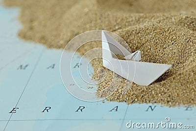 Overturned paper boat on a map with sand - Immigration concept Stock Photo