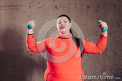 Overweight attractive woman workout biceps on a gray backgaround. Stock Photo