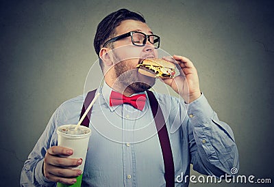 Overweight business man eating with appetite a burger holding a can of soda drink Stock Photo