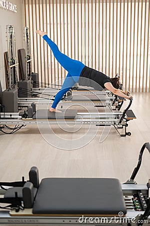 Overweight caucasian woman doing pilates exercises on a reformer. Stock Photo