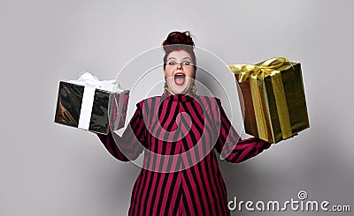 Overweight ginger female in black and purple striped dress and earrings. Holding golden and silver gift boxes, isolated on white Stock Photo