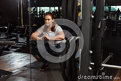 Overweight girl squatting with clenched hands near fitness machine Stock Photo