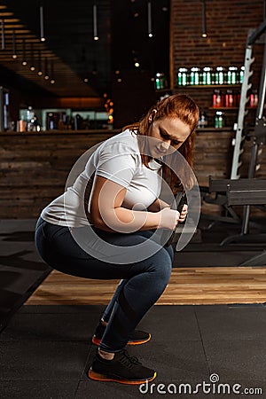 Overweight girl squatting with weight disc in gym Stock Photo