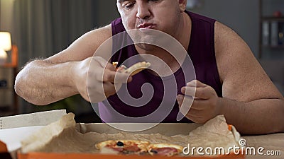 Overweight male eating pizza with delight at night, addiction to unhealthy food Stock Photo