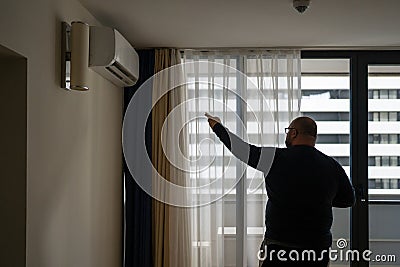 Overweight man switches on air conditioner at home in summer feels abnormally high air temperature. Stock Photo