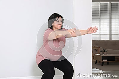 Overweight mature woman squatting near wall at home Stock Photo