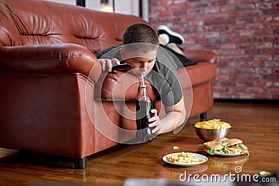 overweight obese boy is drinking carbonated sweet water beverage lying on sofa Stock Photo