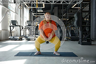 Overweight obese woman squatting with kettlebell while training at gym Stock Photo