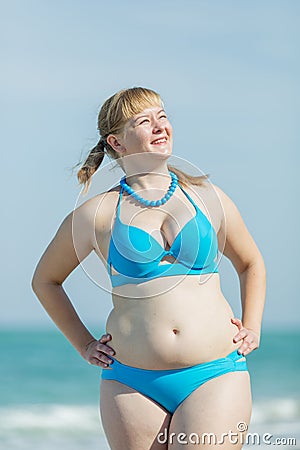 Overweight woman in blue bikini standing arms akimbo outdoors Stock Photo