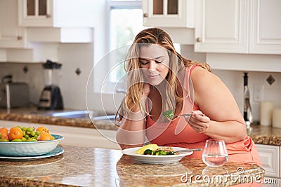 Overweight Woman Eating Healthy Meal In Kitchen Stock Photo