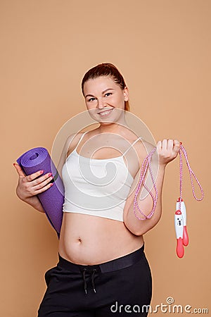 Overweight woman getting in shape. She`s holding a rolled mat and a jump rope Stock Photo