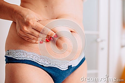 Overweight woman hand holding or pinching fat body belly paunch in bathroom Stock Photo