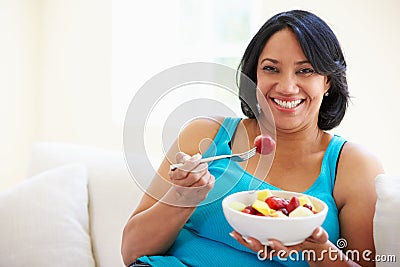 Overweight Woman Sitting On Sofa Eating Bowl Of Fresh Fruit Stock Photo