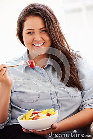 Overweight Woman Sitting On Sofa Eating Bowl Of Fresh Fruit Stock Photo