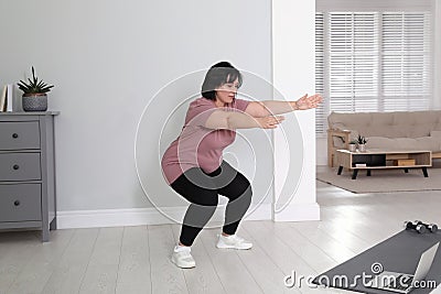 Overweight mature woman squatting while watching online class at home Stock Photo