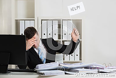 Overworked Accountant Holding Help Sign At Desk Stock Photo