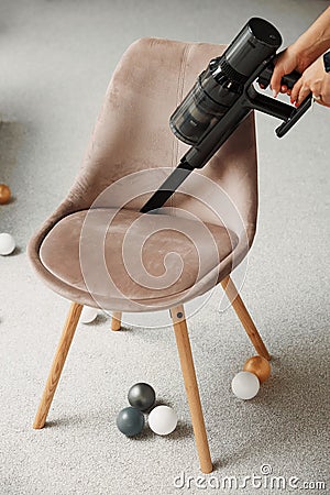 Owner uses handheld wireless vacuum cleaner to clean chair Stock Photo